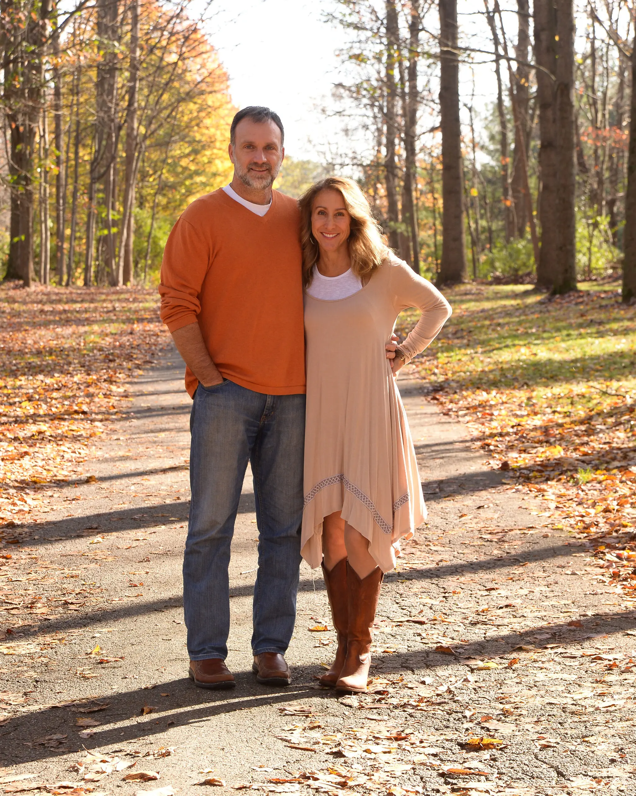 A middle-aged couple standing on a road during fall season.